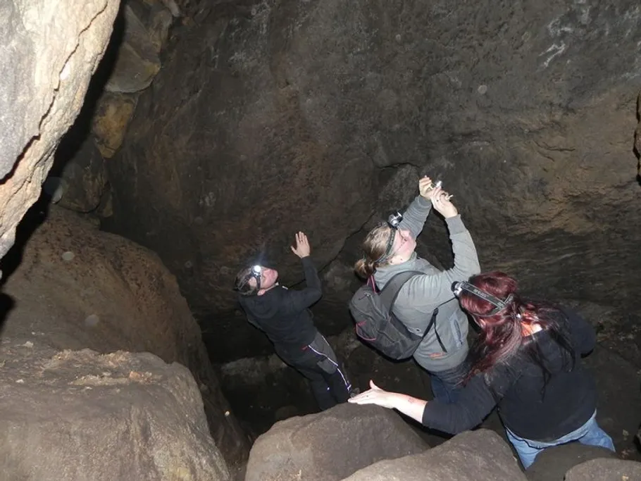 Drei Personen erkunden eine Höhle, tragen Helmlampen.
