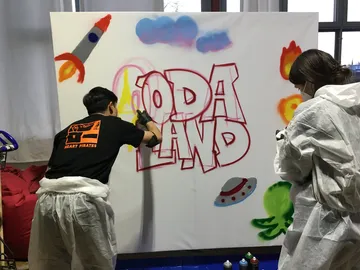 Two people spray colorful graphics onto a canvas.