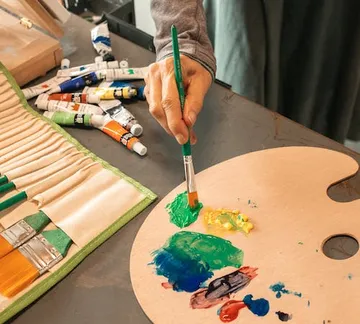 Brush mixes colors on a color palette at the table.
