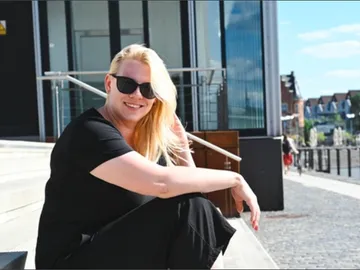 Woman sitting on steps in front of a modern building with a smile.