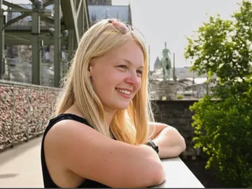 Junge Frau lächelt entspannt auf einer Brücke, sonnig.