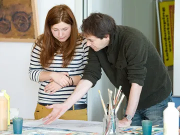 Two people look at a work of art together at the table.