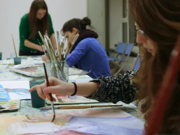Female artists paint at tables in a creative space.