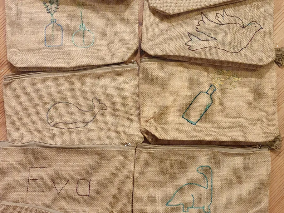 Sechs Stoffbeutel mit bunten Stickereien auf Jute.