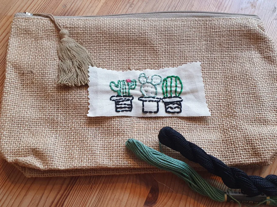 Sackleinenbeutel mit gestickten Kakteen, auf Holzoberfläche.