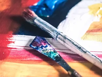 The brush and shovel lie on a lively paint substrate.