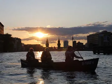 Drei Personen paddeln in einem Boot bei Sonnenuntergang.