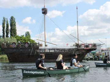 Canoe sails past a big, old ship.