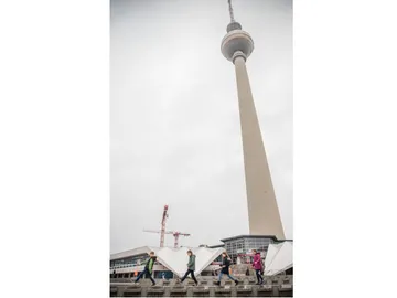 TV tower stands above passing people in grey surroundings.