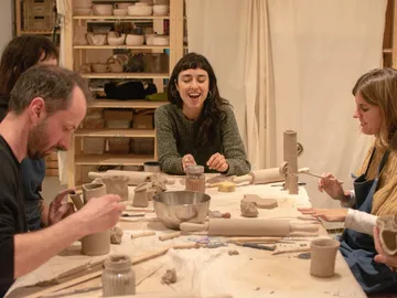 A group of potters is working on various clay objects with a smile.