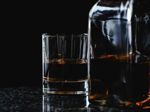 Glas mit dunkelbraunem Getränk steht neben einer Flasche.