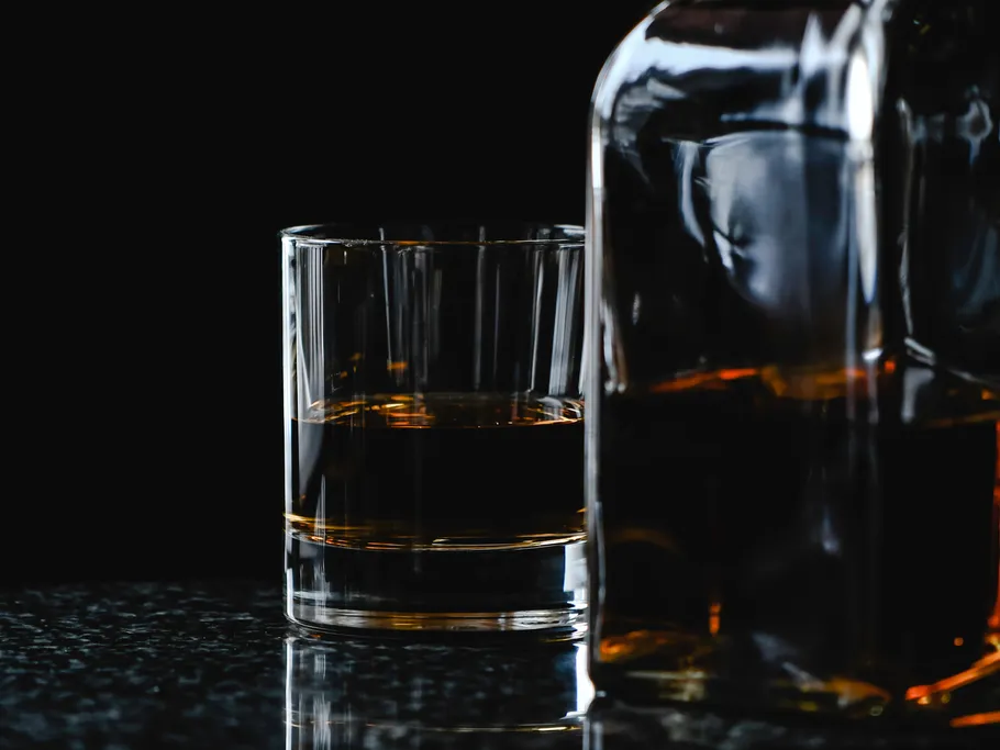Glass with dark brown drink stands next to a bottle.