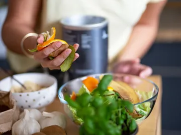 Hand holds fresh vegetables over a bowl in the kitchen.
