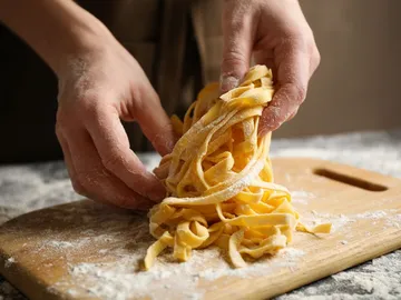 Pasta is formed with hands on a wooden board.