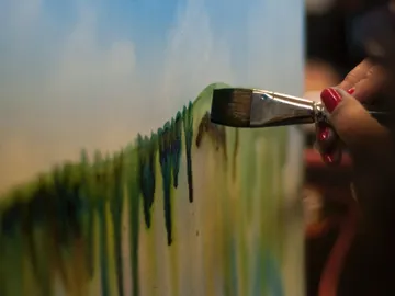 Brush paints green and blue paint on a canvas.