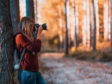 Woman taking pictures in a forest surrounded by trees.