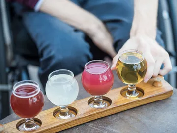 Four drinks on a wooden board, one hand grabs the golden one.