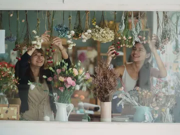 Zwei Frauen dekorieren Trockenblumen in einem Floristikgeschäft.