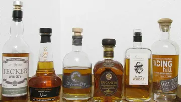 Reihe von Whiskyflaschen steht auf einem Tisch vor Wand.