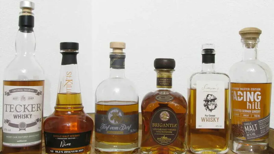 Reihe von Whiskyflaschen steht auf einem Tisch vor Wand.