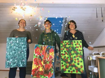 Three women present works of art while confetti falls.