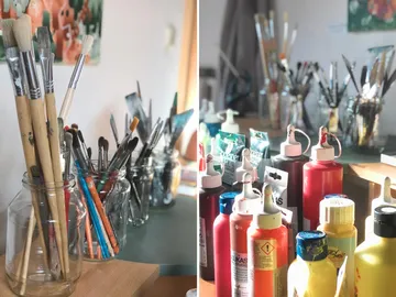 Brushes and paints are on a table in a studio.