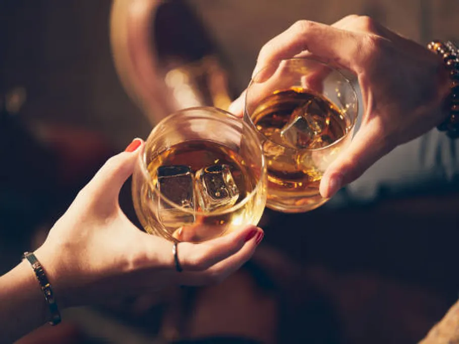 Gläser mit Whiskey stoßen in geselliger Atmosphäre an.