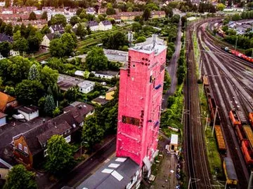 Rosa Gebäude steht neben Gleisen und Wohngebäuden.