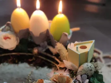 Bunte Ostereier und Kerzen auf einem dekorierten Tisch.