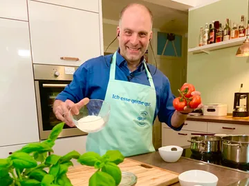 Koch hält Tomaten und Mehl in einer modernen Küche.