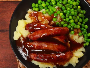 Sausage, mashed potatoes, peas coated with sauce.