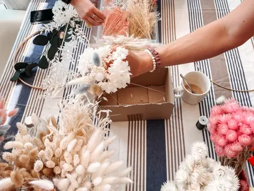 Hände basteln Trockenblumen auf einem Tisch, umgeben von Material.