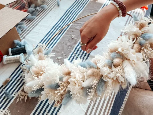 Hand holds a decorative flower wreath on a table.