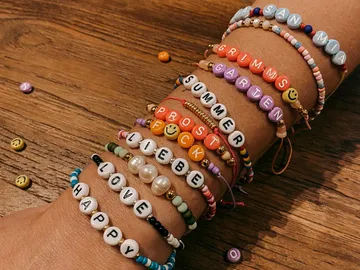 Verschiedene bunte Armbänder schmücken einen Arm auf Holz.