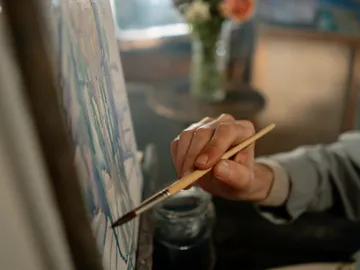 A hand paints on a canvas with a brush.