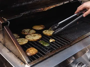 Slices of potatoes are turned over on a grill.