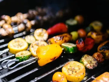 Grilled vegetables lie on an outdoor grill.