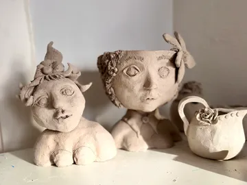 Clay figures stand on a table in front of a wall.