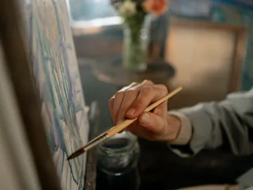 A hand paints on a canvas with a brush.