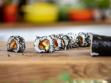 Sushirollen liegen auf einem Holzbrett in einer Küche.