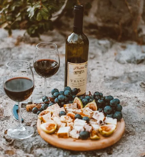 Wine and cheese platter are placed on an outdoor stone table.