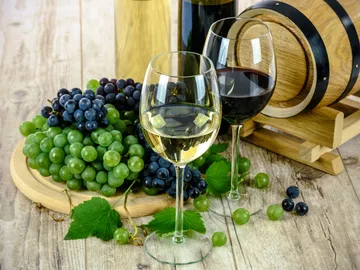 White wine and red wine stand next to grapes on the wooden surface.