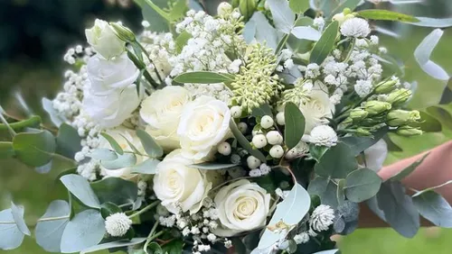 White bouquet is held by one hand, outdoors.