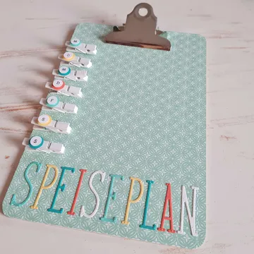 Clipboard mit Essensplan und farbigen Clips für Wochentage.
