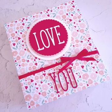 Geschenkbox mit floralem Muster, bunt verziert und beschriftet.