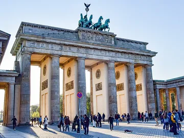 Brandenburger Tor steht, Menschen gehen darunter, sonniger Tag.