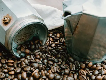 Coffee beans are strewn next to a moka pot.