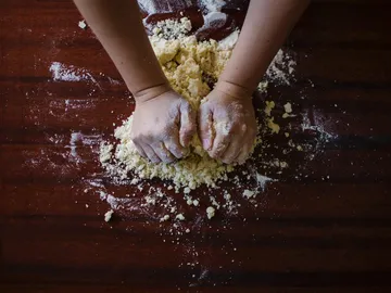 Hands knead dough on a wooden plate with flour.
