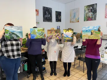 Five people hold paintings in an art studio.