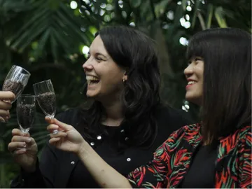 Three women with glasses make a toast in a green environment.